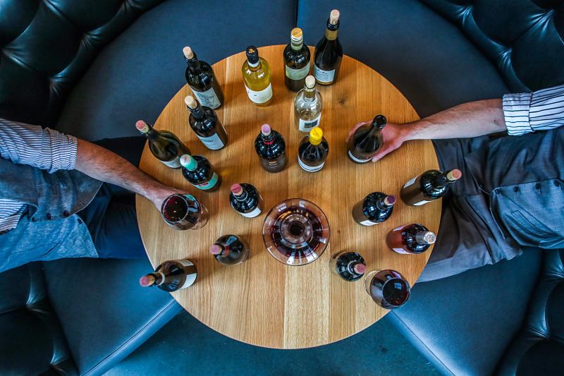 Mesa redonda vista desde el techo llena de botellas de vino mientras dos hombres catan los vinos en la tienda de bebidas en Salamanca de Comercial Williams