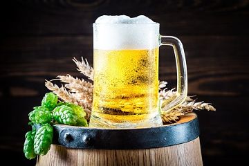 Jarra de cerveza sobre un barril de cerveza, en el barril hay tambien un poco de lúpulo y trigo