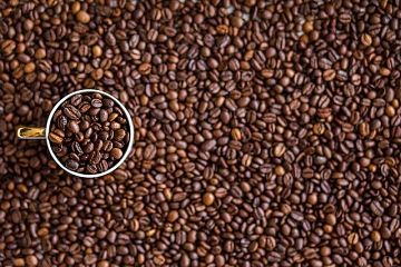taza llena de granos de café, a su alrededor más granos de café